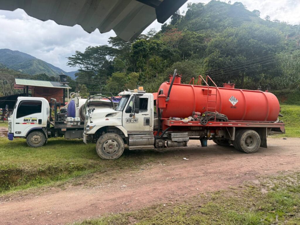 Dos camiones cisterna para transporte de aguas, uno pequeño y otro grande con tanque rojo, estacionados en un camino de tierra en zona rural de Cundinamarca